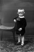 Ateljébild på en pojke bredvid en pall. Enligt Walter Olsons journal är bilden beställd av fru Vivi Cederquist.