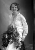 Ateljébild på en kvinna med blommor hängandes runt halsen. Enligt Walter Olsons journal är bilden beställd av fröken Ingrid Andersson.