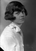 Ateljébild på en kvinna med ondulering och rosett. Enligt Walter Olsons journal är bilden beställd av Britta Dunge.
