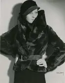 Modell i pälsjacka med skärp och hatt.