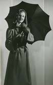 Modell i kappa med kapuschong, handskar och paraply.