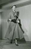 Modell i klockad kjol, jacka och knytblus, hatt, handskar och pumps, från Dior.