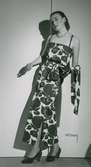 Modell i stormönstrad klänning med slits och midjeband, pärlhalsband och pumps, från Edward Molyneux.