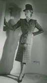 Modell i rutig dräkt, hatt med hög kulle och pumps.