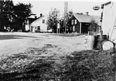 Torget i Brunn i mitten av 1920-talet.
Det vita huset är affär där nuvarande Konsum efter ombyggnad finns. Timmerhuset med vita knutar inrymde lager till affären samt färdstall och bostadsrum på övre våningen. Rivet i slutet av 1920-talet. Det vita huset till höger innehöll affär, läkarmottagning och bostad och finns ännu kvar i ursprungligt skick (1985). OBS ! den primitiva oljeförsäljningen.