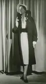 Modell i klänning, kappa, hatt, handskar och pumps. Från Jacques Fath.