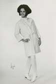 Mannekäng i kappa och byxor i vit jersey, platta skor och hatt. Originalmodell från André Courrèges, NK:s Franska, höst 1962.