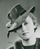 Modell i hatt med kulle och brätte, hattband trätt genom kullen.