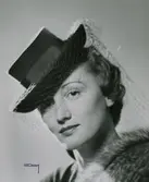 Modell i hatt med kulle och brätte med upvikta kanter. Hattband och flor.