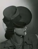 Modellen och skådespelerskan Hjördis Genberg  i hatt med kulle. Brättet uppvikt bak, rosett i ena sidan.