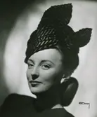 Modell i hatt av draperat randigt tyg. Två snibbar av tyget upprättstående.