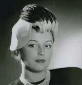 Porträtt av modell i gul filthatt med fantasi och flerradigt pärlhalsband. Från Madame Paulette.