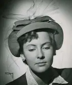 Porträtt av modell i tapaye-gul filthatt, uppsvängda brätten på sidorna. Av Maud Roser.