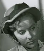 Porträtt av modell i grå filthatt med dubbelt brätte, svart bandmontering och flor. Av Rose Descat.