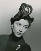 Porträtt av modell i stråhatt av Madame Paulette, samt brosch och örhängen.