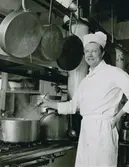 Man i kockkläder och mössa rör i en gryta. påskrift med blyerts på baksidan: 