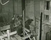 Fem män på en byggnadsställning. Text med blyerts på baksidan: 