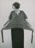 En kvinna håller ut sidorna med knytband på en triangulärt formad tröja med zick-zackmönster. Nordiska Kompaniet.
