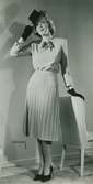Modell i veckad kjol och tröja med rosett i halsen, handskar, pumps och hatt av Edward Molyneux.