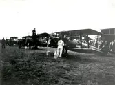 Orig. text: Flygets dag på  flygfältet i Malmslätt. F3 Jaktfalkar iordningställles för uppstigning.

Extern upplysning: Flygplanen på bilden är inte J6 Jaktfalk utan Sk11 Tiger Moth.

Extern upplysning 2025-09-15: Tyvärr är det inga Sk 11 heller (men nära på), det är ett besök från Norge och deras Flyveskole med De Havilland 82 Tiger Moth. Tydlig norsk Haerens Flyvevåpen märkning på rodret. Serienummer ser ut att vara 153 och 157 för de två närmaste.