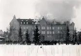 Orig. text: Linnéskolan brinner 22 feb. 1923. 

Gnistor från en kamin antände en intilliggande vedtrave varvid en omfattande brand uppstod i skolbyggnaden.
Linnéskolan sedd från Torkelbergsgatan. Skolan byggdes 1896-98. 1983 blev skolan vårdgymnasium och fick namnet Birgittaskolan. Efter branden fick skolan nytt utseende.