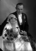 Bröllopsbild. Kvinnan har brudsklänning och brudslöja. Håller i en bukett blommor. Mannen håller i ett par handskar. Beställare till bilden: Helge Jakobsson ifrån Kalmar.