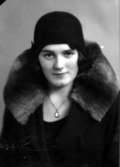 Ateljébild på en kvinna med medaljong, hatt och kappa. Enligt Walter Olsons journal är bilden beställd av Saga Hjalmarsson.