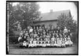 Vedevågs skola, 69 skolbarn med lärare.
Skolbyggnad i bakgrunden.
Folkskolläraren P.G. Larsson