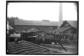 Fabriksbyggnad, industriområde, ånglok med vagnar, byggnader och arbetare.
Tegelmästare J.P. Andersson