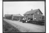 En och en halvplans bostadshus, en flygelbyggnad.8 personer framför huset.Ludvig Andersson.