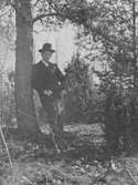 John Bauer står lutad mot en tall i skogen.