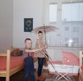 Syskonen Lars-Åke (gift: Dahlén) och Ilse (gift: Glimberg) Jansson har fått eget rum år 1967. 3-årige Lars-Åke håller en dockvagn och 7-åriga Ilse ett paraply. Familjen har precis flyttat till en ny modern lägenhet i Tynnered efter att ha bott omodernt och trångt i Krokslätt.