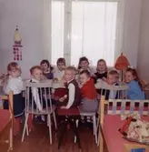 Barnkalas för Lars-Åke Jansson (gift Dahlén) som fyller 4 år 1964. Han är iklädd hängslen, röd tröja och grå byxor. I bakgrunden från vänster sitter storasyster Ilse med mörka hårtofsar, okänd, Claire och Anette Larsson. Familjen bodde 1 år i Tynnered och kalaset firas i barnens gemnsamma rum.