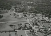 Flygfoto över Fågelfors, samhälle med villor och bostadshus samt åkrar och skog.