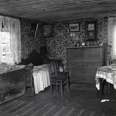 Interiör från boningshusets stora rum. Rummet sett från köket. Fars chiffonier och säng. Vid gavelfönstret ett slagbord.