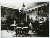 Interiören av Hantverkshuset år 1908. Det finns bord, piano, soffa och väggmålningar.