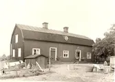 Södra flygeln mot gårdsplanen. Till vänster lång svale = nergång till mejeriet i källarvåningen. Panelat rött timmerhus under brutet tak.
