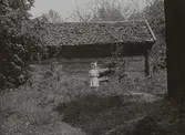 Flicka framför knuttimrad bodbyggnad.
