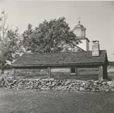 Ryggåsstuga i Stenåsa. Kyrkan syns i bakgrunden.