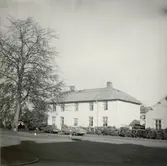 Bostadshus med staket, barn, bilar och ett träd.