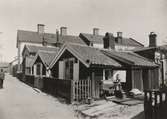 Små bostadshus med fönsterluckor och träfasader på Västerlånggatan i Gamla staden år 1908.