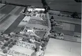 Flygfoto över Åby. Byn med jordbruk, ladugård och ekonomibyggnader samt hus och åkrar och vägen genom byn.