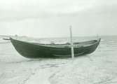 Båt fastgjord vid i flisan nersatt stång för att icke tagas av sjön. Denna strandflisa som översköljes av vågorna kallas 
