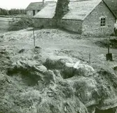 Klumpstenar och hällar över en hällkista. I bakgrunden syns smedjan.