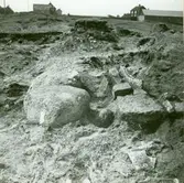 Klumpstenar och hällar över en hällkista. I bakgrunden syns smedjan.