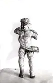 Skulpturen är en putto. En allegorisk liten amorin som ofta ingick som staffage i altaruppsättningar eller (ännu vanligare) på orgelfronter. De hade i sina händer olika ikonografiska föremål som tydliggjorde sammanhangen

Konservator Sven Wahlgren 1939.