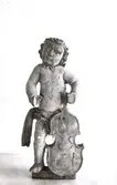 Skulpturen är en putto. En allegorisk liten amorin som ofta ingick som staffage i altaruppsättningar eller (ännu vanligare) på orgelfronter. De hade i sina händer olika ikonografiska föremål som tydliggjorde sammanhangen.