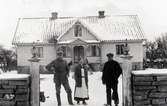 John Petersson och hustrun Elna framför mangårdsbyggnaden på sin gård. Personen till höger okänd. Troligen är det drängen på gården.