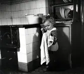 Lilla Rita vid vedspis och diskbalja.