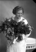 Ateljébild på en kvinna som håller i en blombukett i konfirmationssammanhang. Enligt Walter Olsons journal är bilden beställd av Arne Lindén.